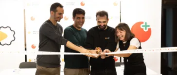 Four people cut a celebratory ribbon together, smiling, at an event backdrop with logos and a Playable Factory sign in the background.
