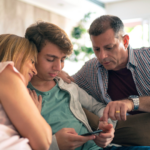 Three adults on a sofa, huddled together and looking at a smartphone.