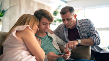 Three adults on a sofa, huddled together and looking at a smartphone.