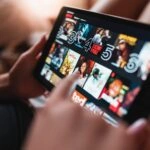 yousafbhutta-tablet-7025855 – mobile marketing reads Close-up of a tablet screen showing a grid of movie posters in a streaming app, with a hand interacting with the display
