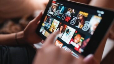 Close-up of a tablet screen showing a grid of movie posters in a streaming app, with a hand interacting with the display